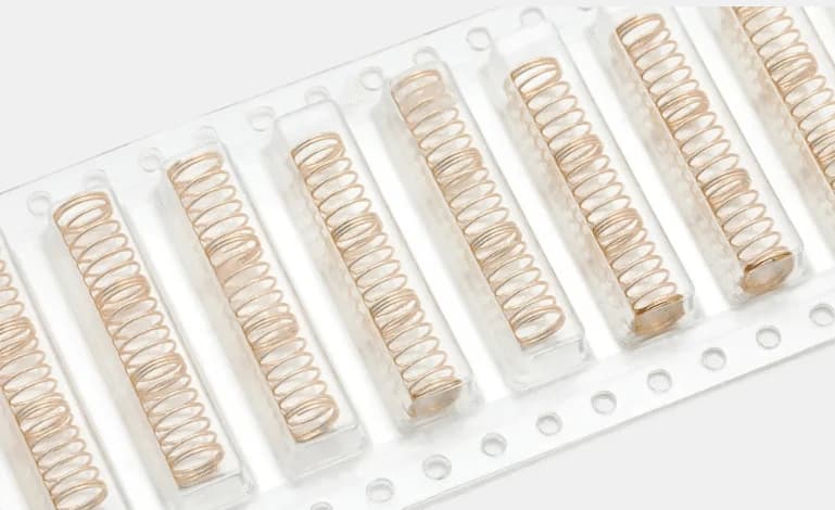 Gold-colored switch springs in packaging, each with three open-coiled sections separated by closely wound bands.