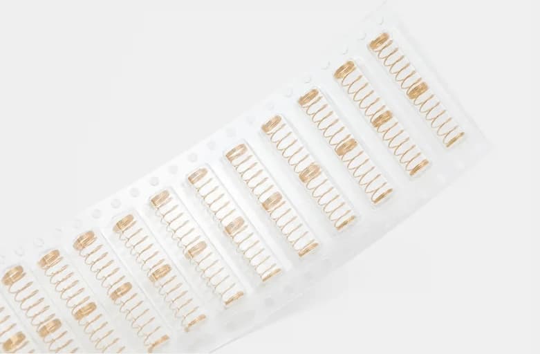Gold-colored switch springs in packaging, each with two open-coiled sections separated by a closely wound band.