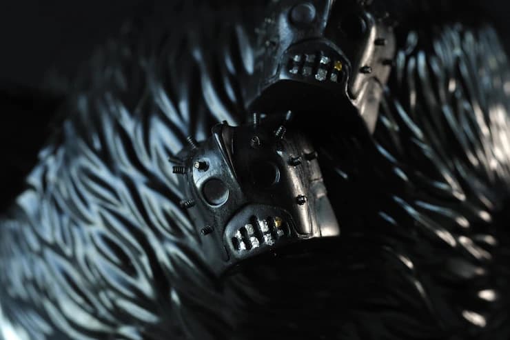 Two dark Baba Yaga Pinhead artisan keycaps with protruding black metal pins and exposed teeth on a ridged black surface.